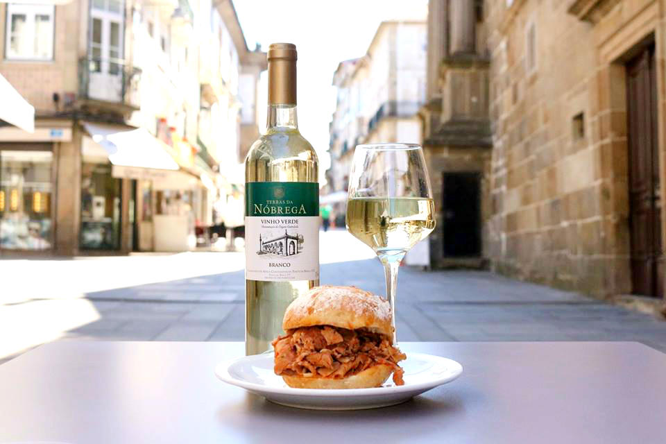 Foto de garrafa e copo de Vinho Verde com bifanas em pão.