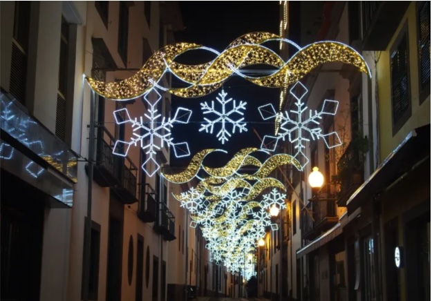 Rua iluminada no Funchal com decorações natalícias compostas por flocos de neve e ondas douradas, criando um ambiente festivo e encantador.