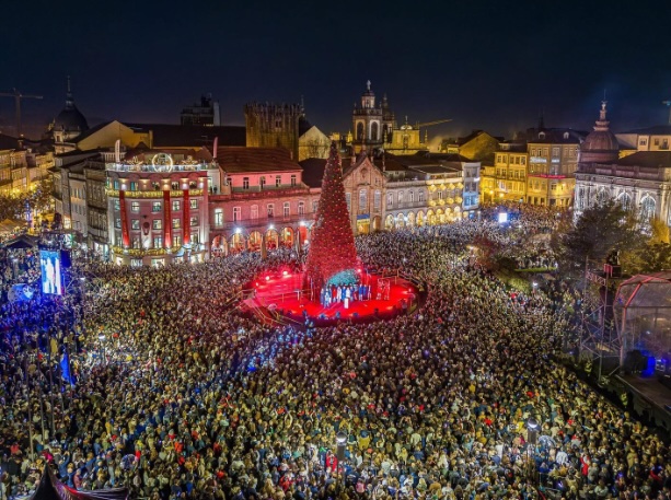 Estrutura iluminada em forma de castelo no centro de Viseu, decorada com luzes brancas brilhantes, rodeada por árvores com decorações luminosas e pessoas a desfrutar do ambiente festivo.